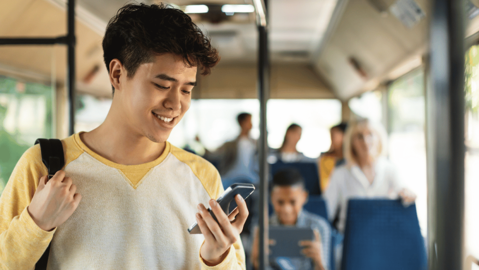 young person stood on a bus looking at phone